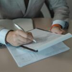 Close-up of business person signing documents at a desk with a pen.